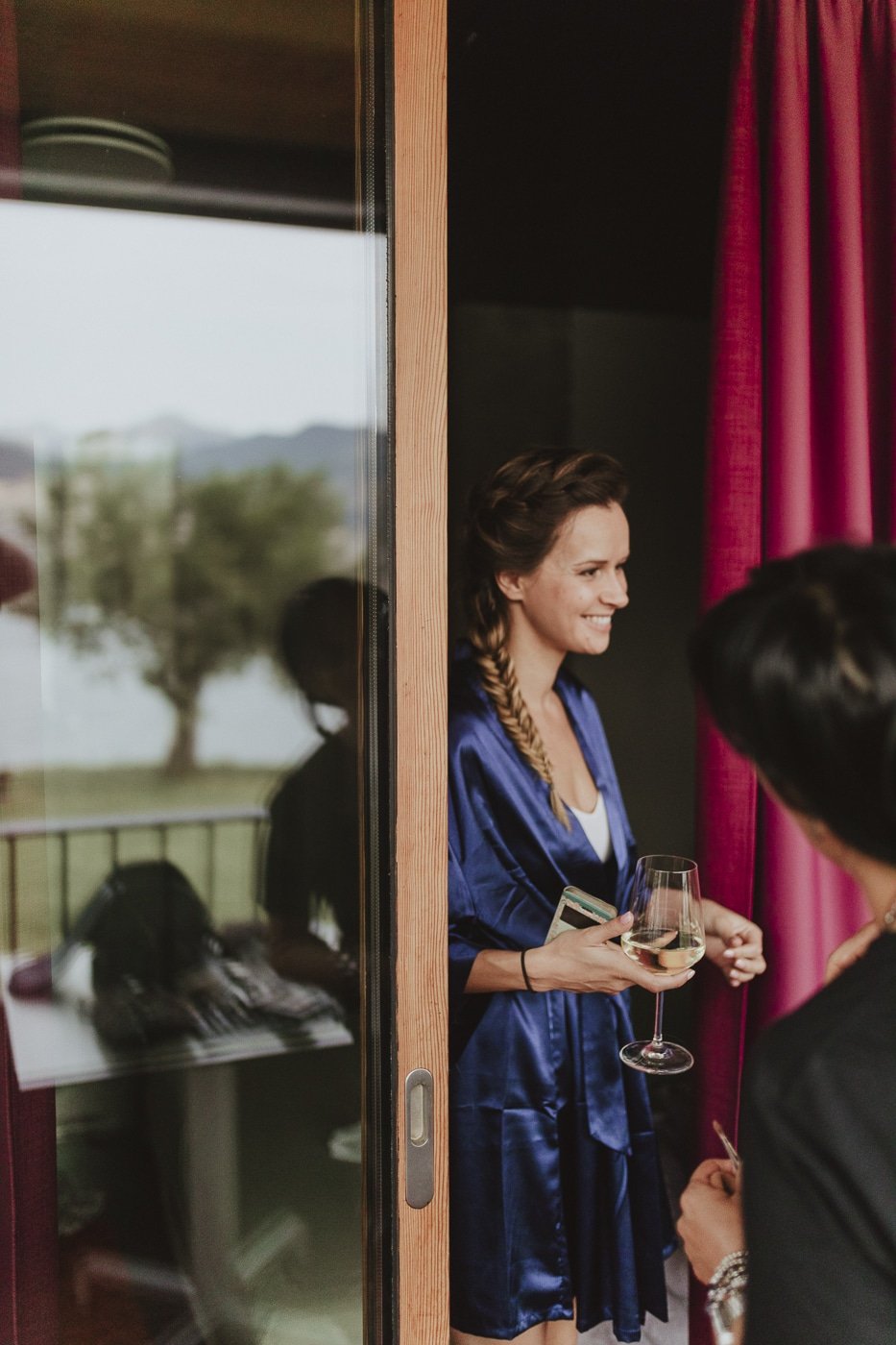 Bridesmaid walking through door wearing blue robe and carrying glass of wine