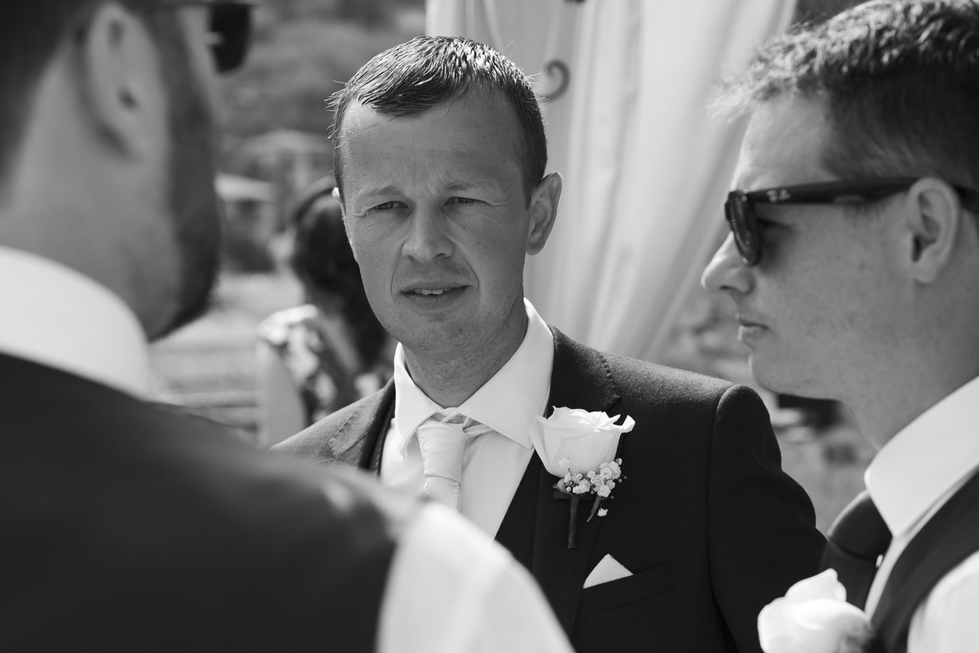 Groom with flower in his lapel talking to men with sunglasses on