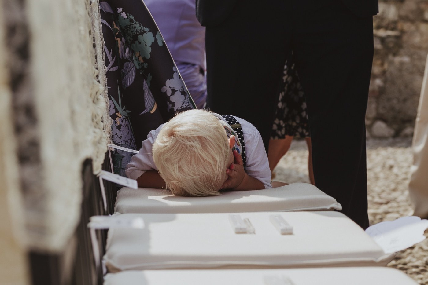 Small blond boy laying on cushioned seat behind guests
