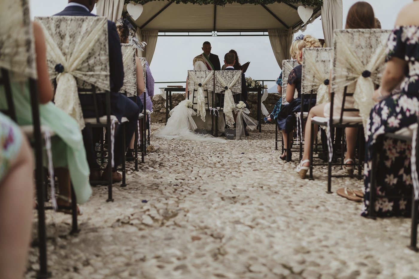 Looking down the aisle at the bride and groom sitting at the front during their wedding vows overlooking the lake