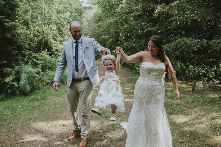 A post wedding portrait session capturing a bride and groom walking with their daughter in the woods.