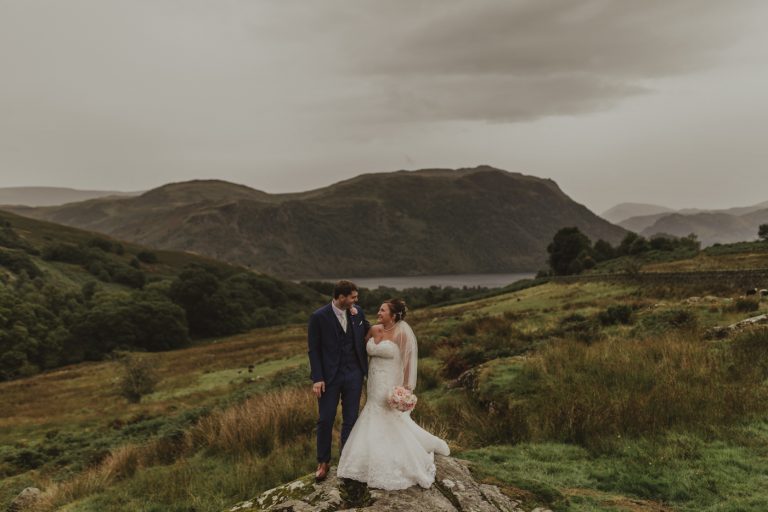 A bride and groom standing on top of a rock in Heather Glen Country House, located in the lake district.