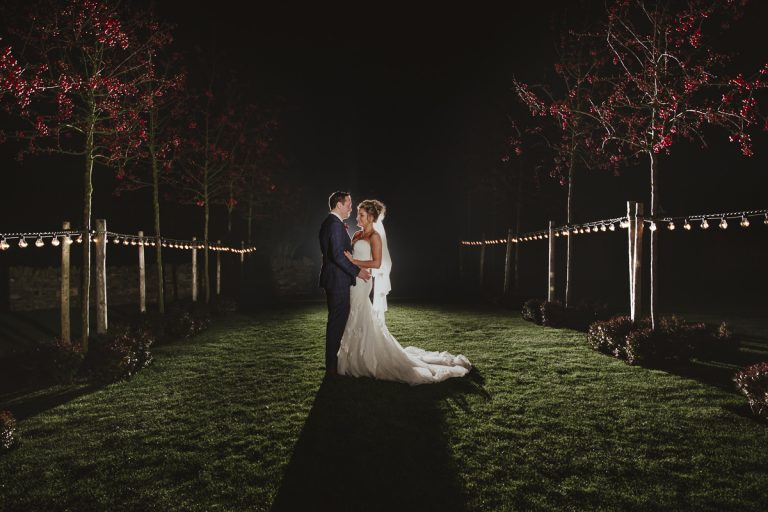 A bride and groom standing in a field at Healey Barn at night.