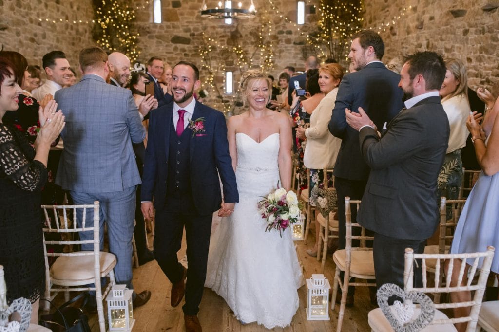 A man and woman walking down the aisle at Three Hills Barn.