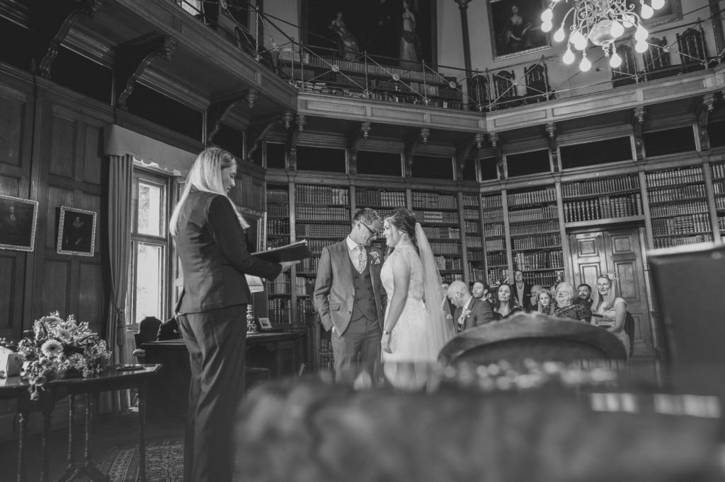 A black and white photo of a bride and groom in a library, captured with the assistance of an Additional Photographer.