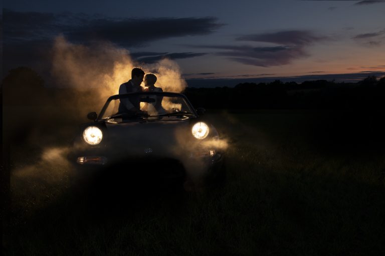 An outdoor wedding ceremony with a couple sitting in a car at dusk.