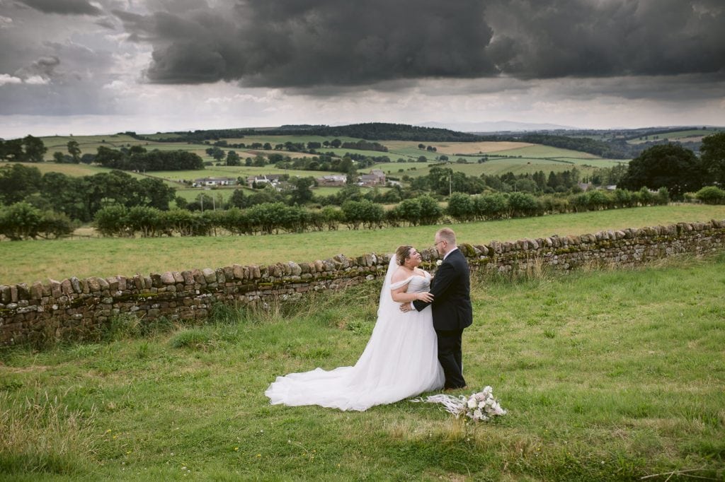 A Heather Glen wedding with a bride and groom standing in a field under a stormy sky.