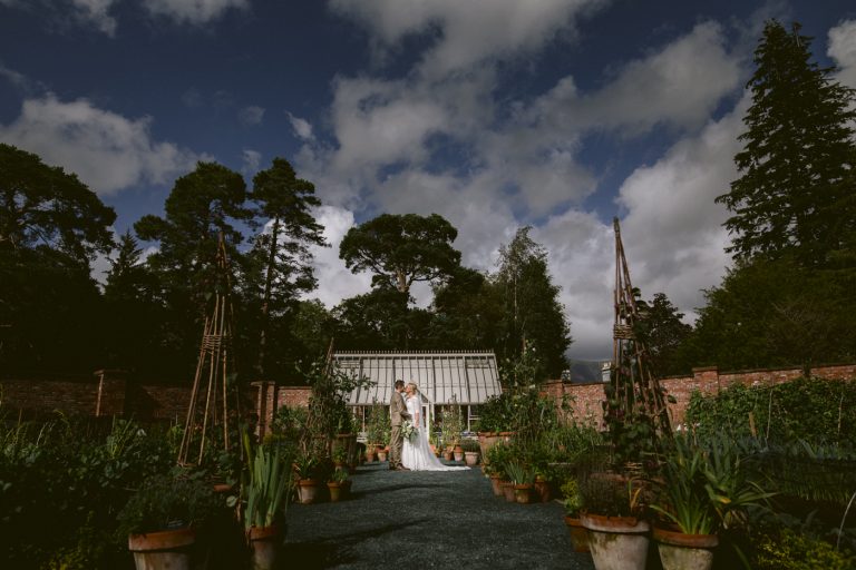 A Lingholm Estate Wedding featuring a bride and groom standing in a garden under a cloudy sky.