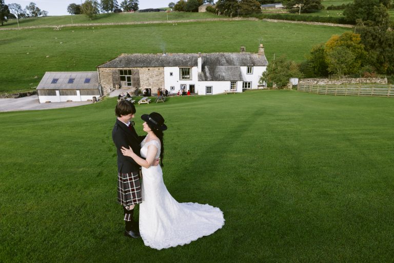 A Knipe Hall wedding featuring a bride and groom in kilts, standing on a grassy field.
