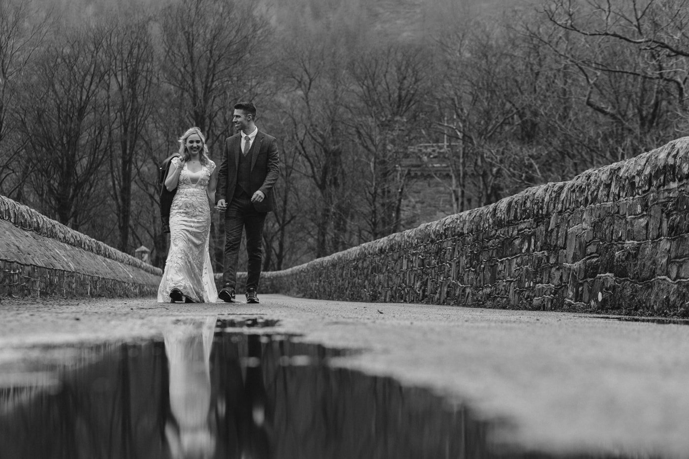 Post wedding portrait session of a bride and groom walking on a bridge, captured in a black and white photo.