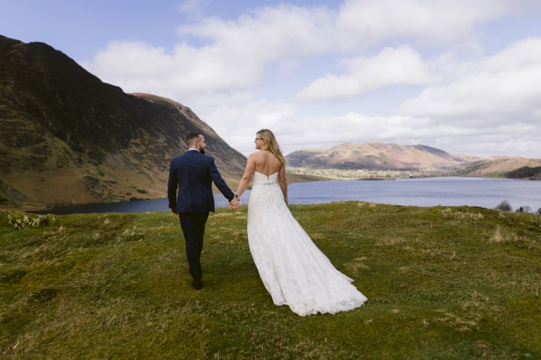 A newly married bride and groom posing for a post wedding portrait session, with a picturesque hilltop view of a serene lake in the background.