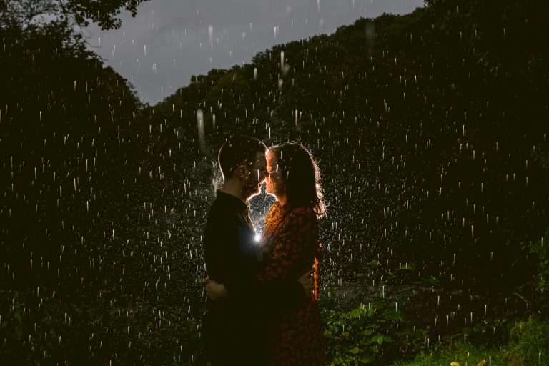 A couple kissing in the rain under a Hidden River Cabin.