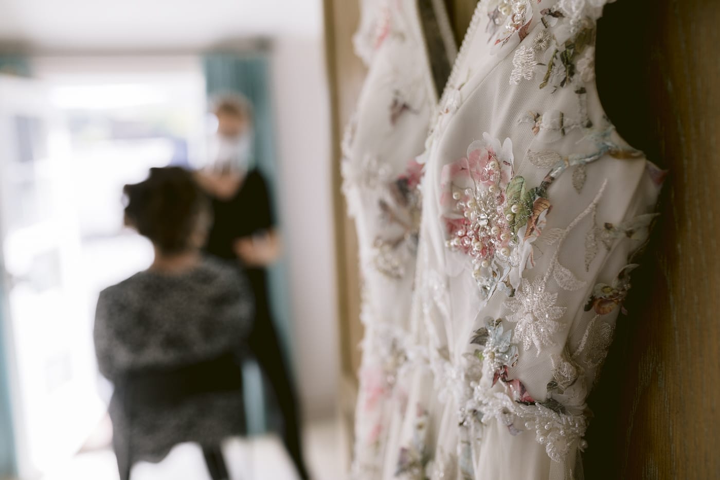 A stunning Hexham House wedding dress hangs gracefully on a hanger in a beautifully lit room.