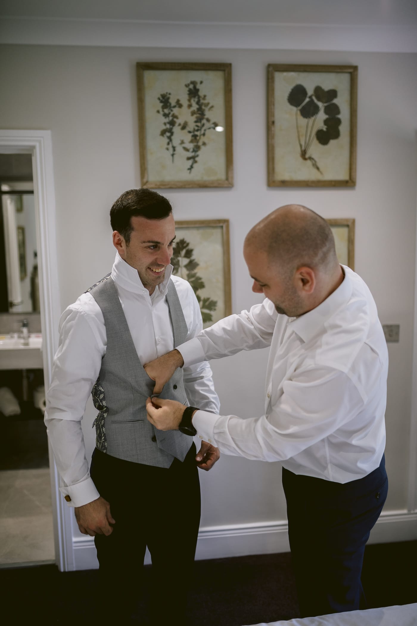 A man preparing for a Hexham House Wedding, expertly putting on a tie in front of a mirror.