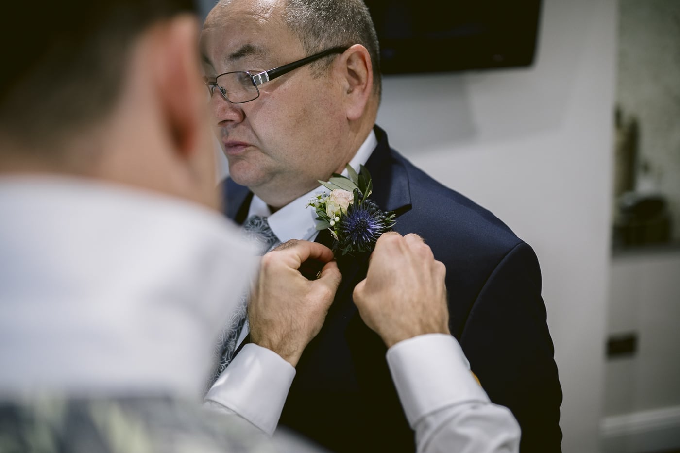 A man in a suit is adjusting his boutonniere at Hexham House Wedding.