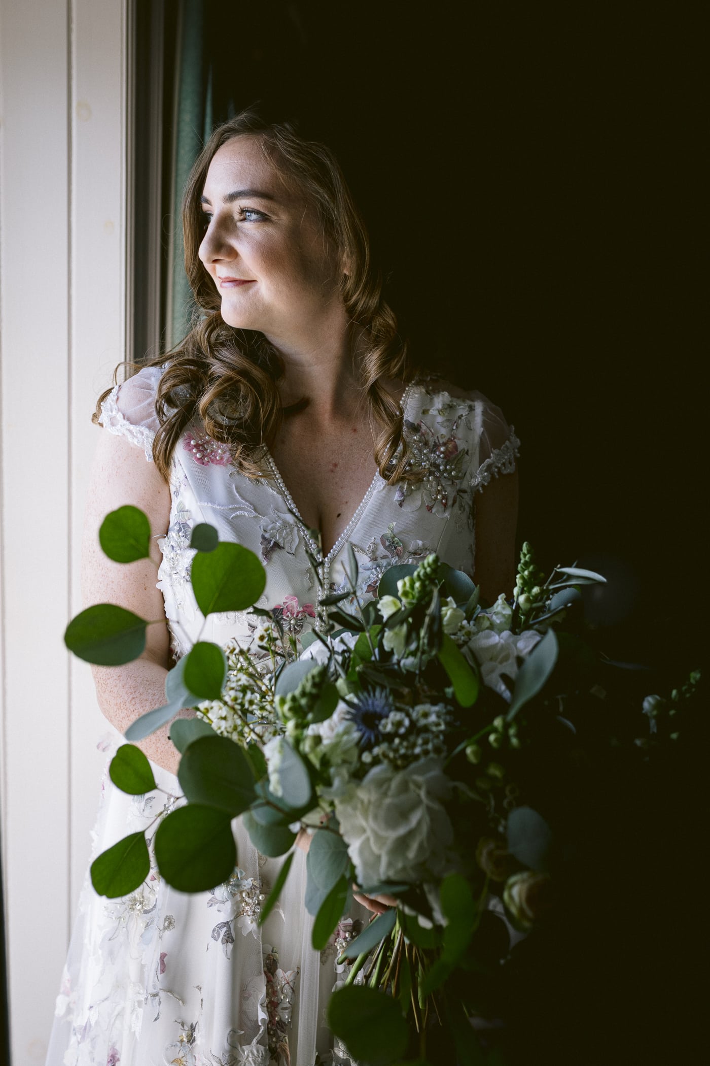 A Hexham House bride holding a bouquet in front of a window during her wedding.