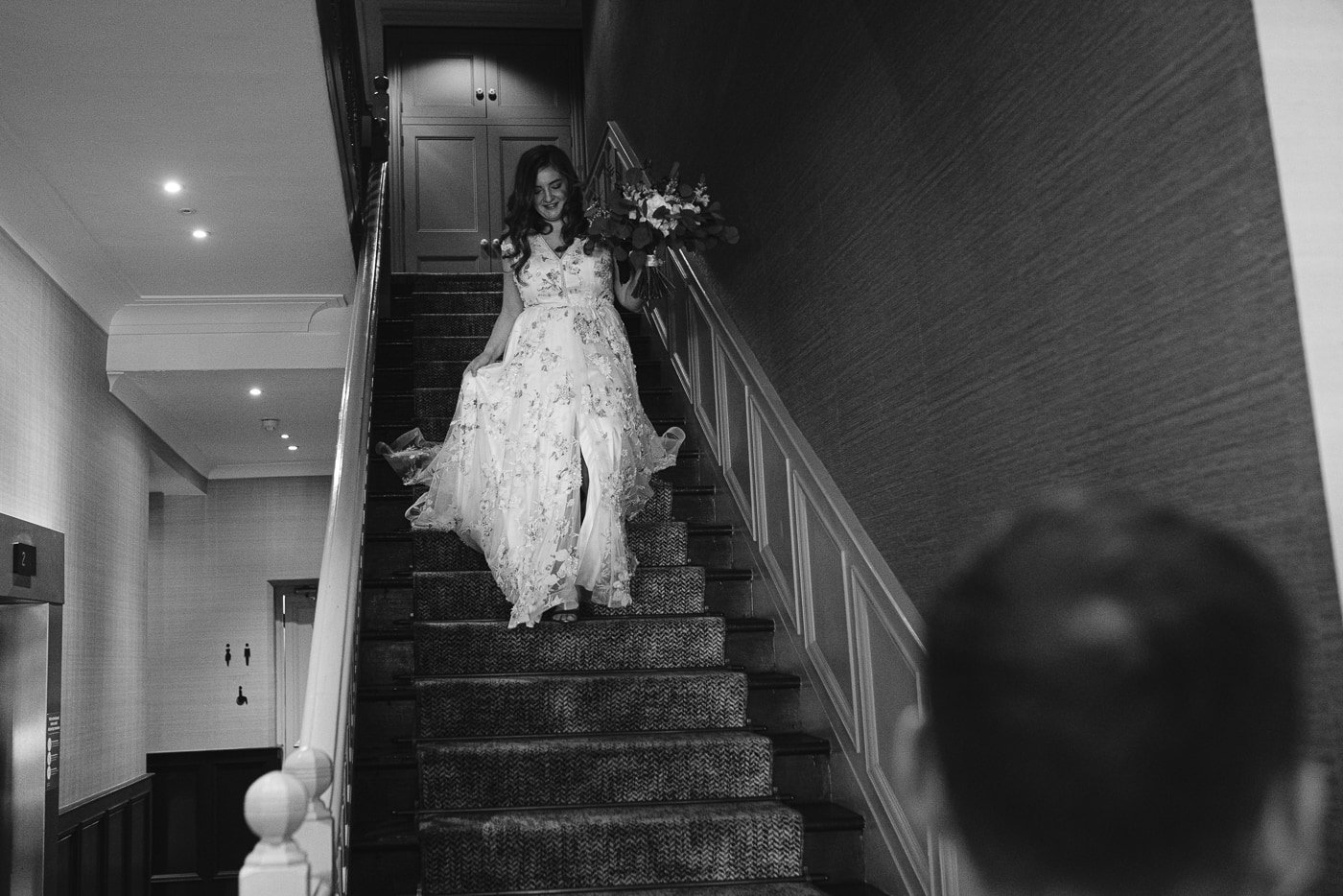 A bride is gracefully descending the stairs of Hexham House in her exquisite wedding dress.