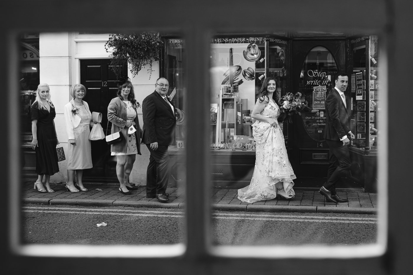 A black and white photo of a Hexham House wedding party in front of a shop window.