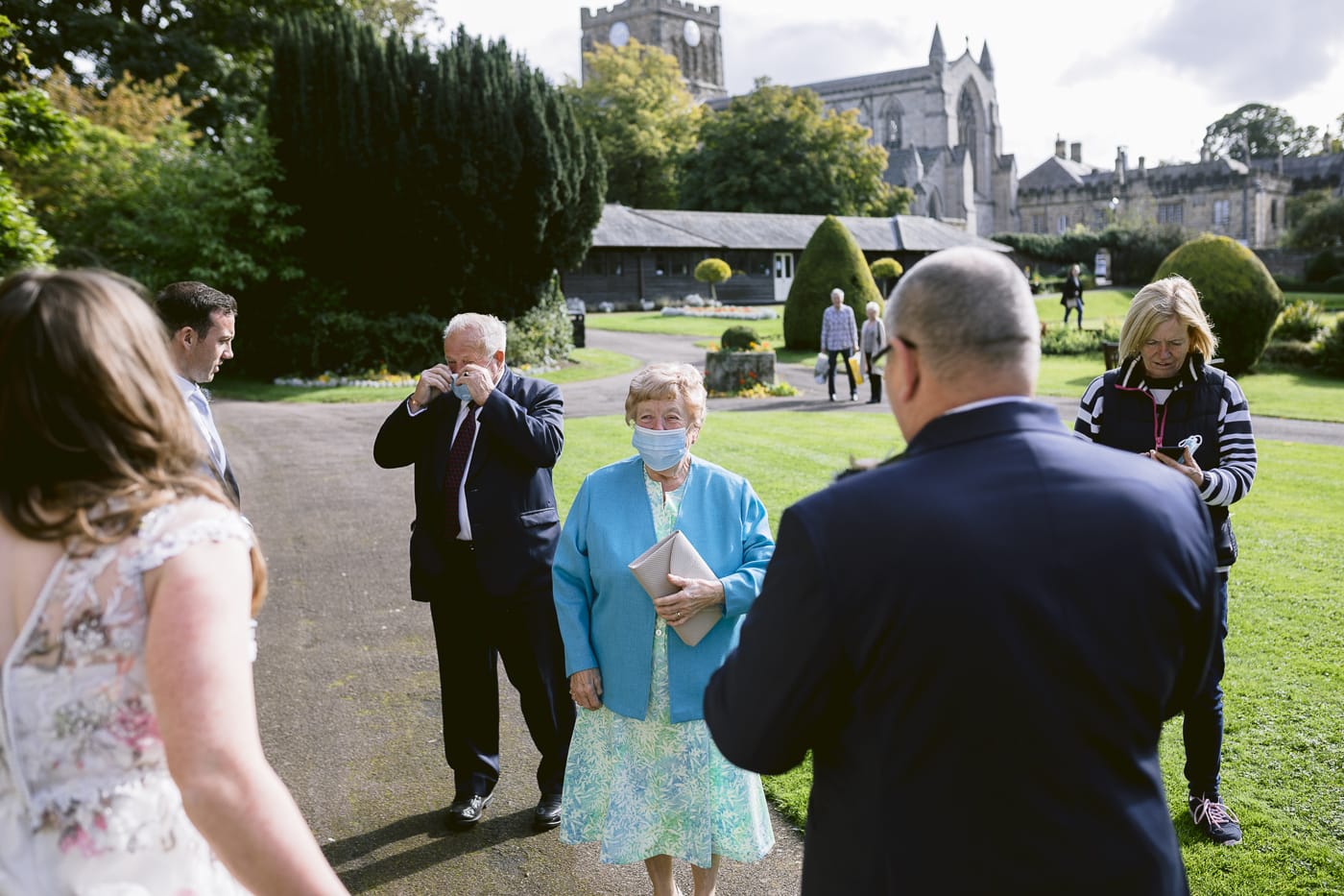A group of people standing in Hexham House garden with a man wearing a mask during a wedding.