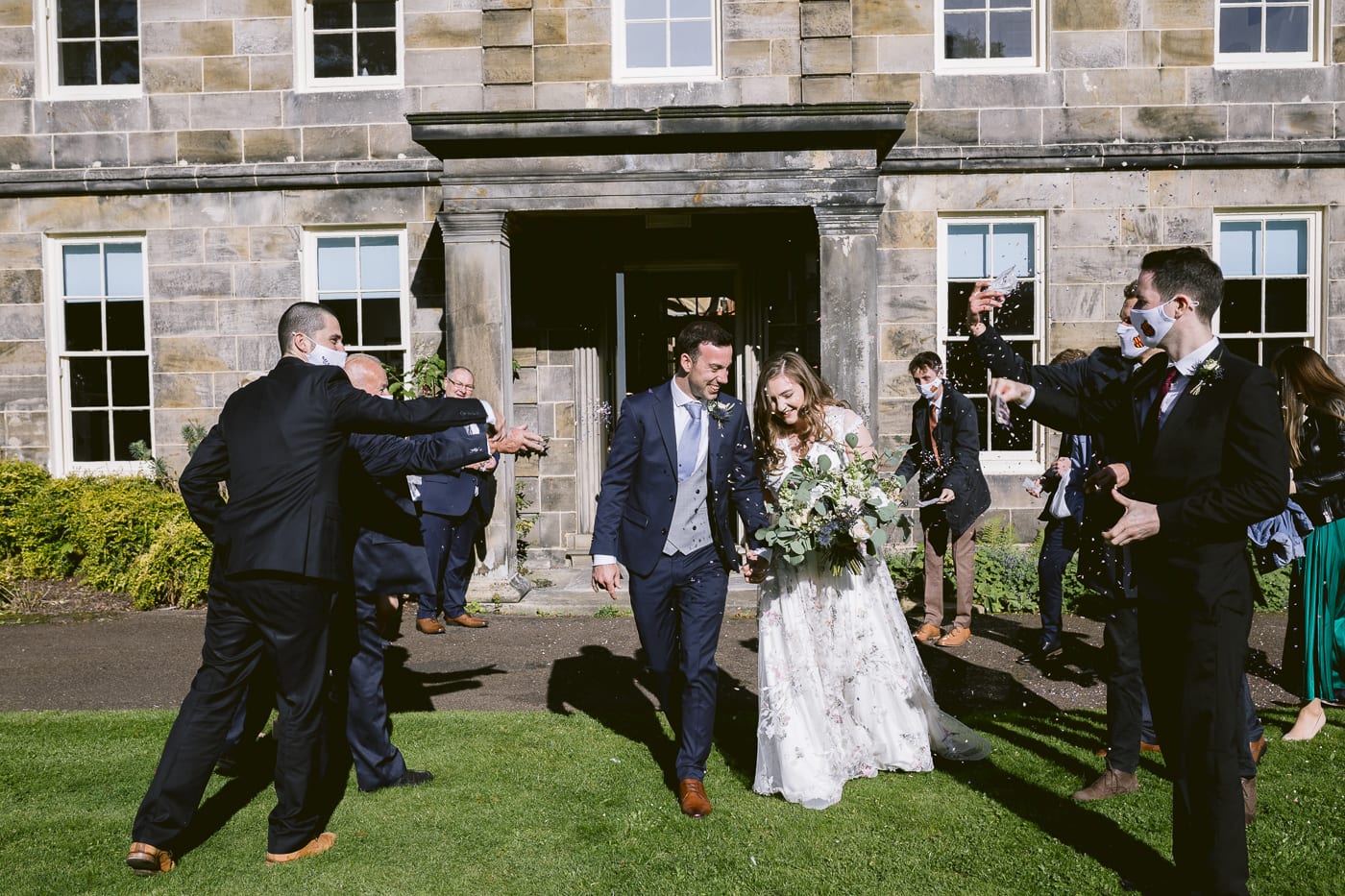 A group of bridesmaids and groomsmen gracefully exit Hexham House, a beautiful mansion, after attending a memorable wedding.