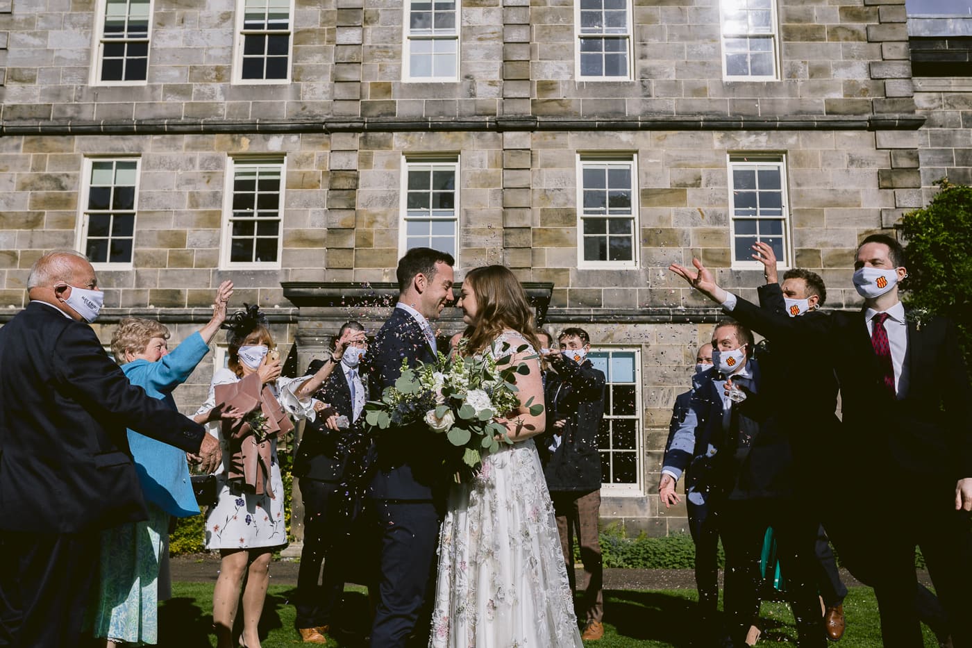 A bride and groom are throwing confetti in front of Hexham House on their wedding day.