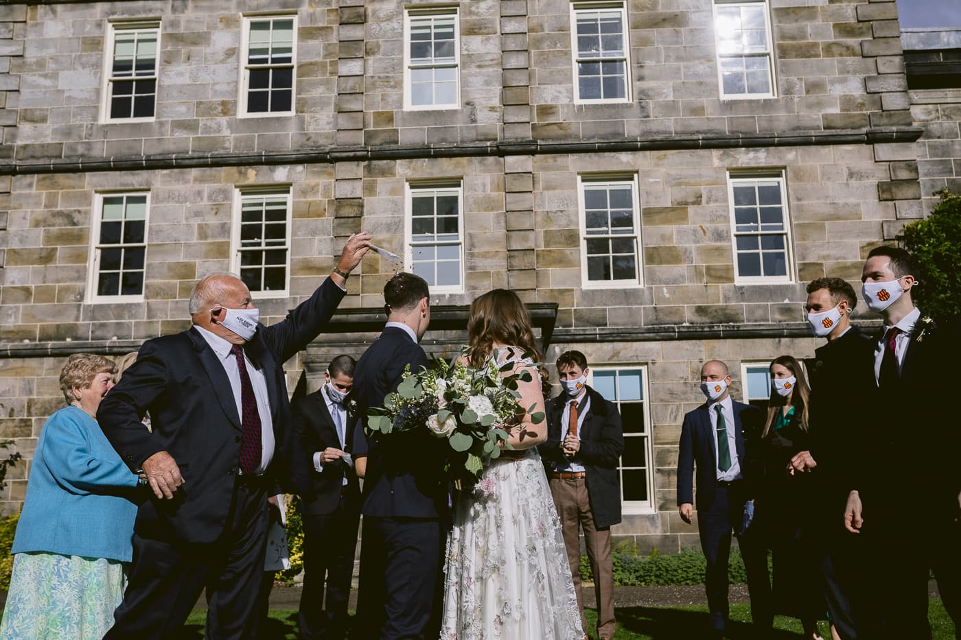 A Hexham House wedding party wearing face masks in front of a large building.