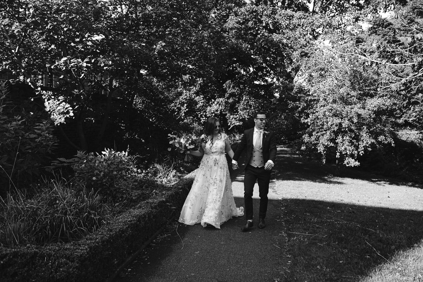 A black and white photo capturing the charming Hexham House Wedding, as a bride and groom joyfully walk down a scenic path.