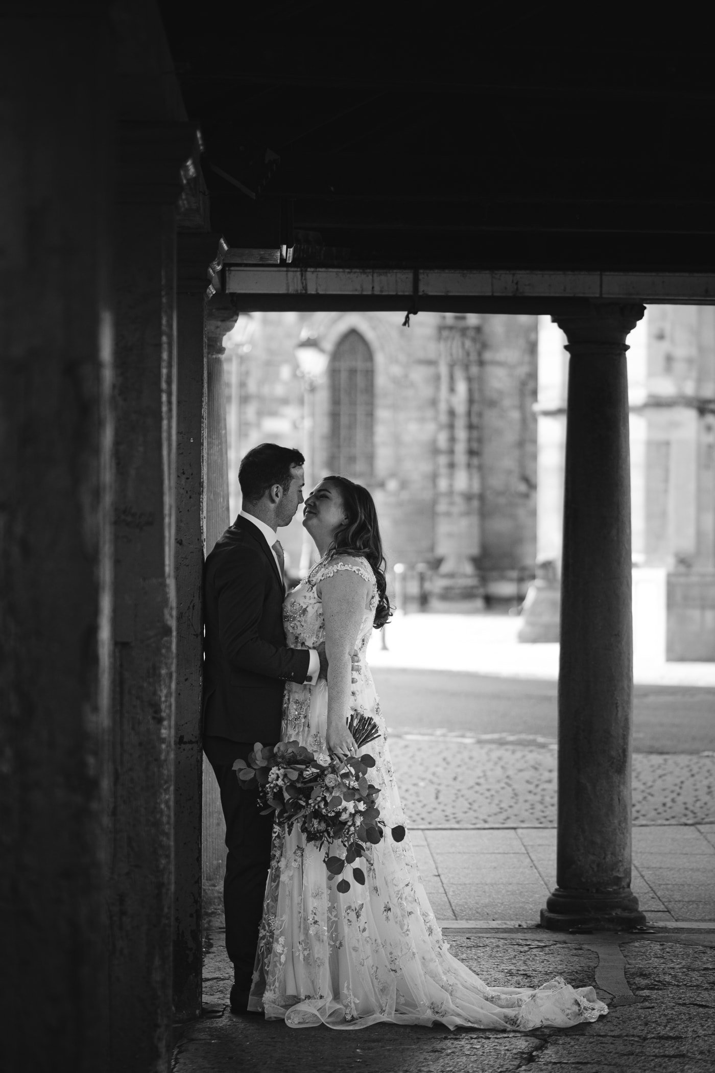 At Hexham House Wedding, a stunning bride and groom share a heartfelt kiss beneath an elegant archway.