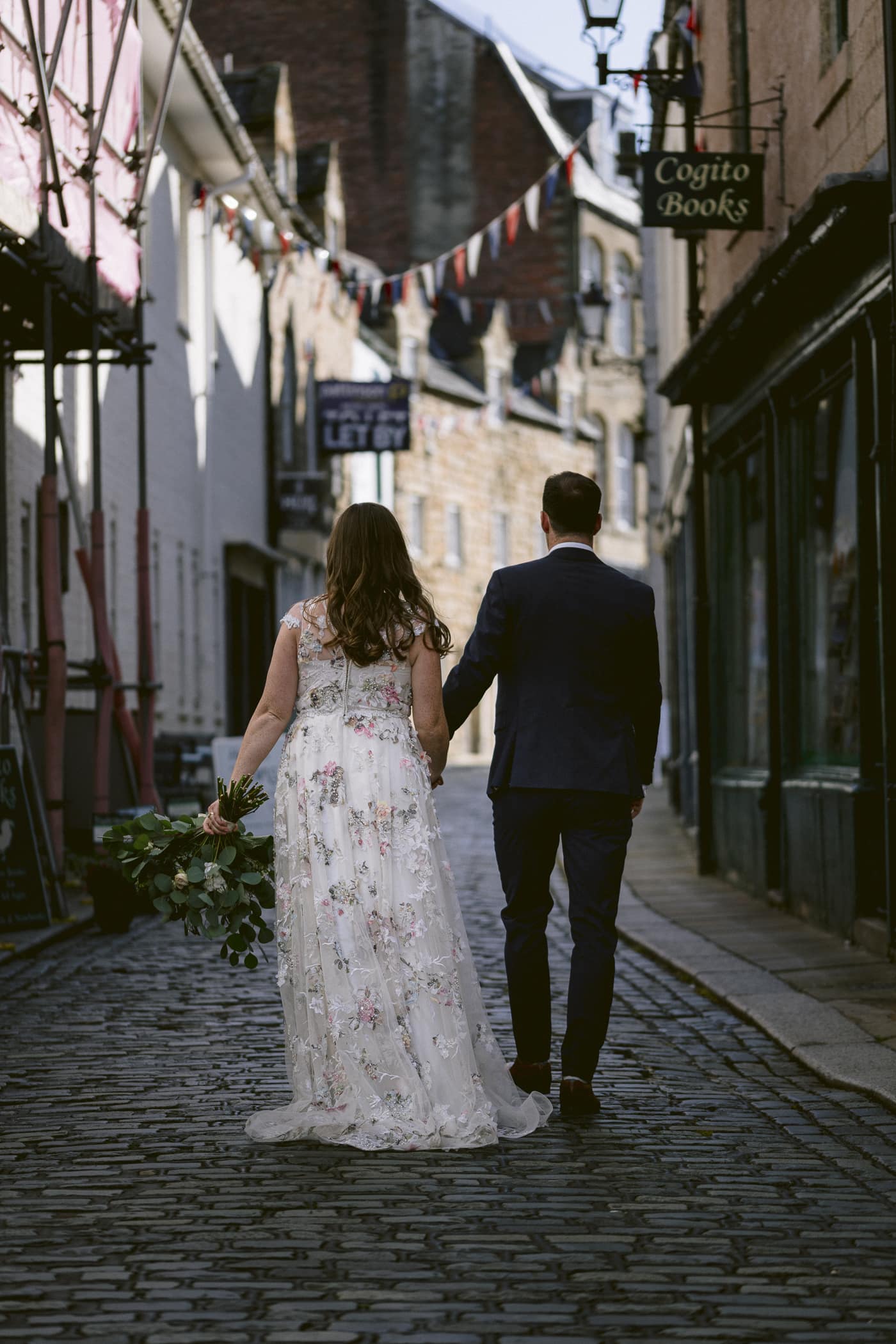 A Hexham House Wedding - A stunning bride and dashing groom walking hand in hand down a picturesque cobblestone street.