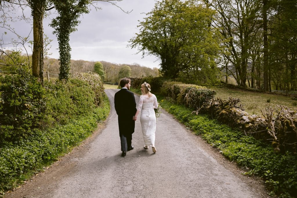 An intimate bride and groom walking down a country road during their Lake District church wedding.