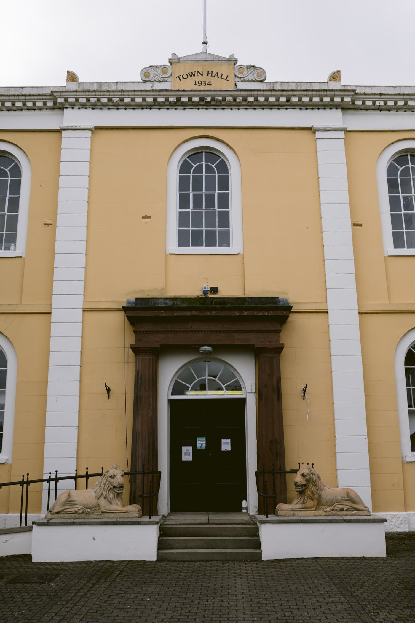 A yellow building adorned with lion statues stands in the serene backdrop of the Lake District.
