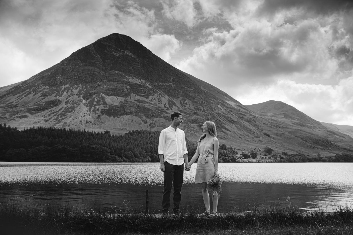 A couple standing in front of a lake with mountains in the Lake District.