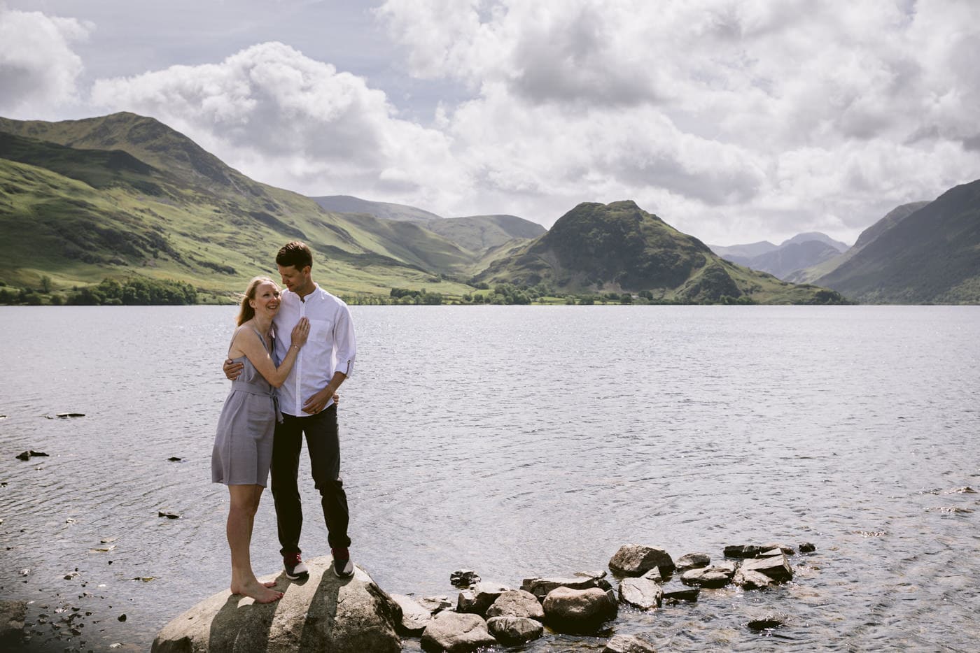 A Lake District couple standing on rocks near a lake with mountains in the background celebrate their Civil Partnership.