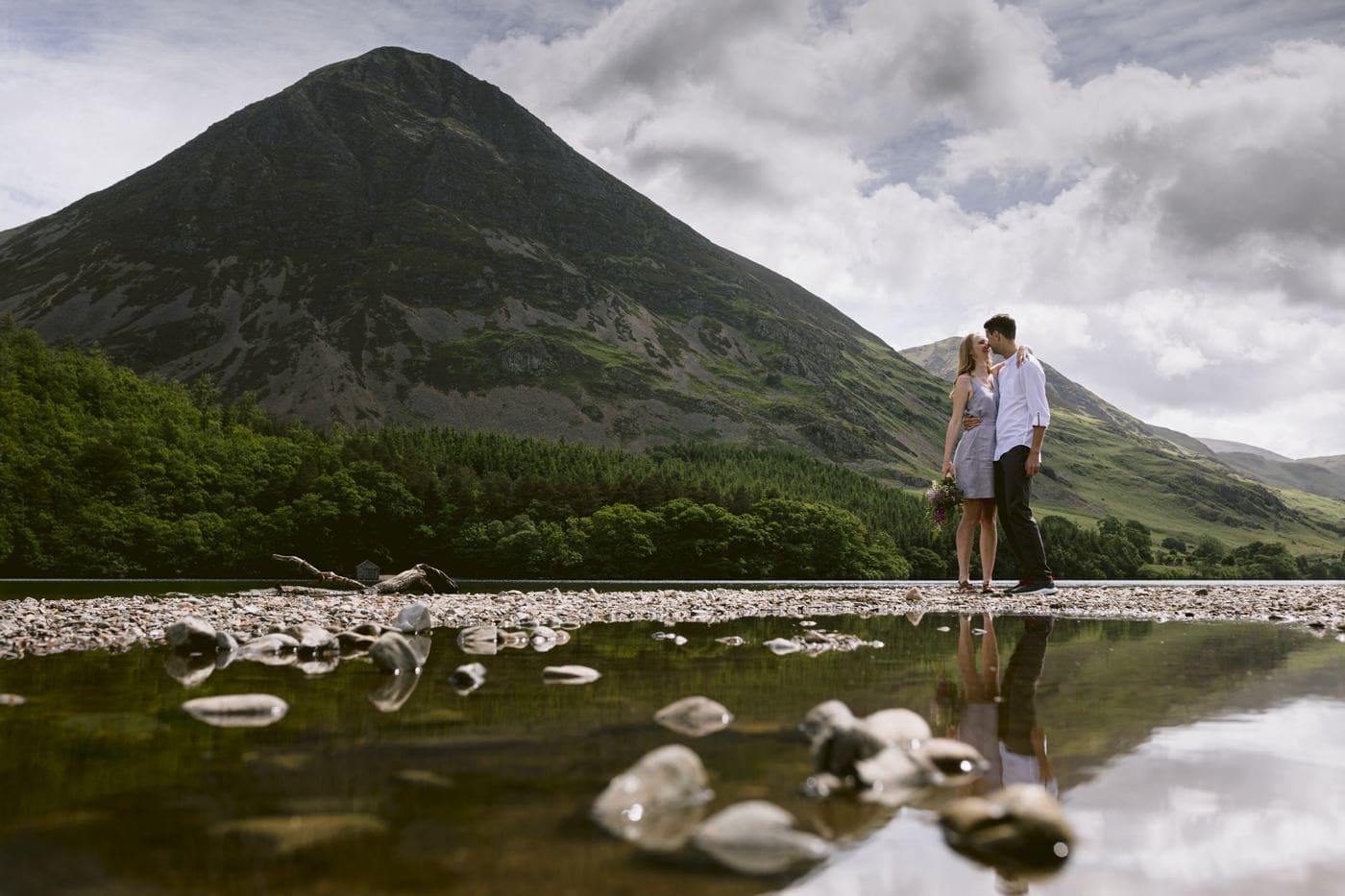A couple standing next to a lake in the Lake District with mountains in the background.