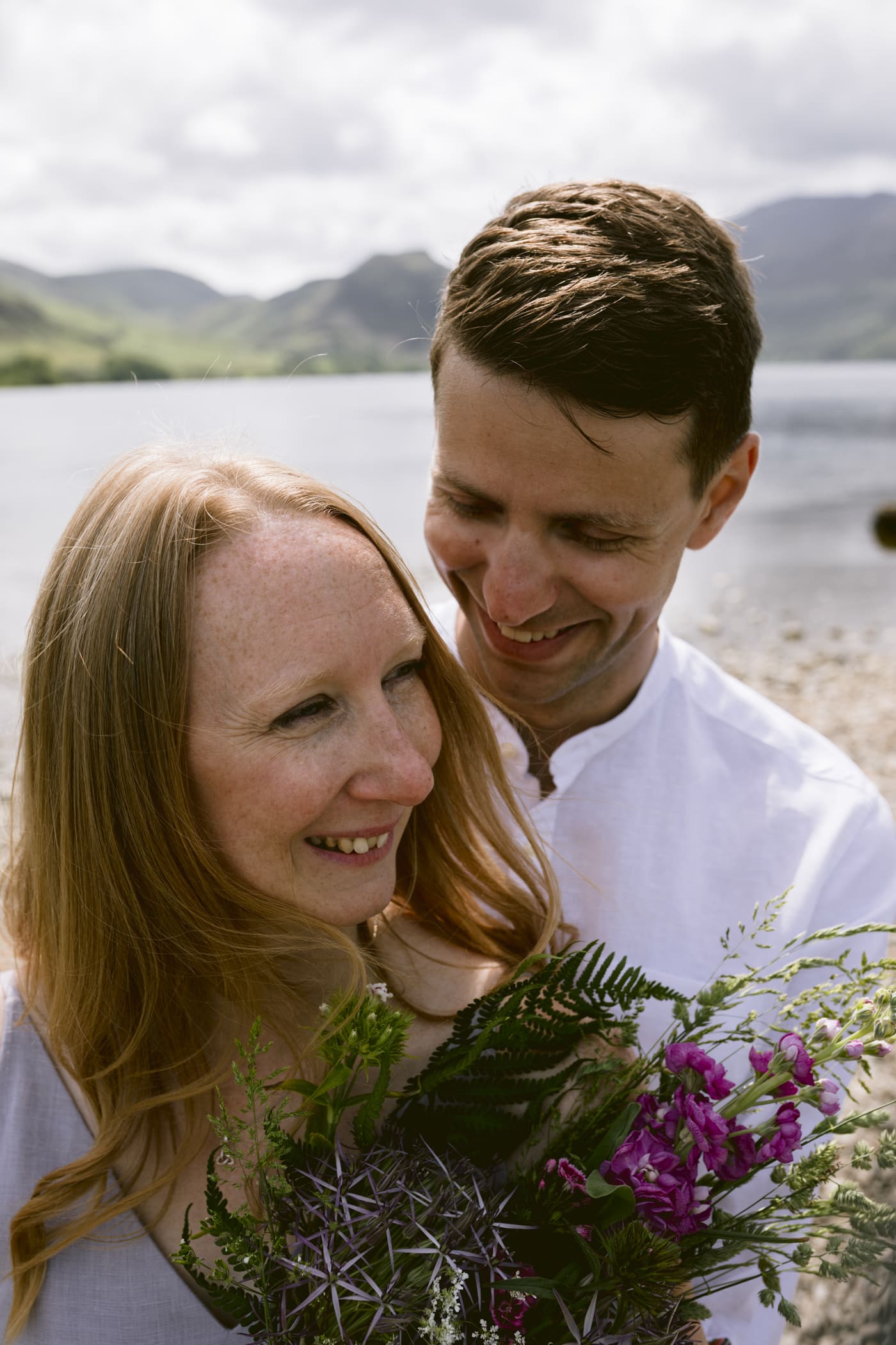 A couple holding a bouquet of flowers on the shore of Loch Ryan, Lake District.