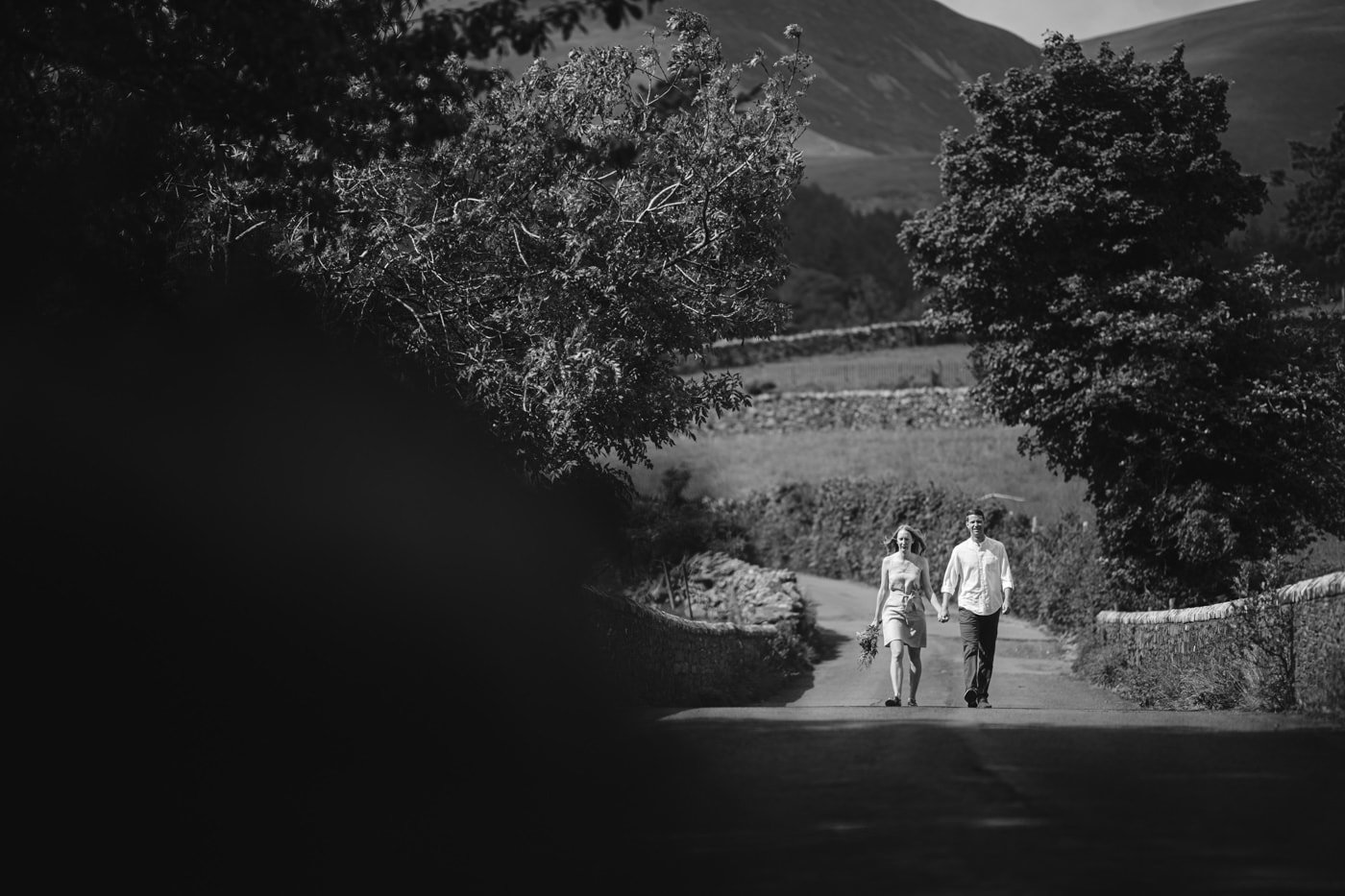 A black and white photo of a couple walking down a road in the Lake District.