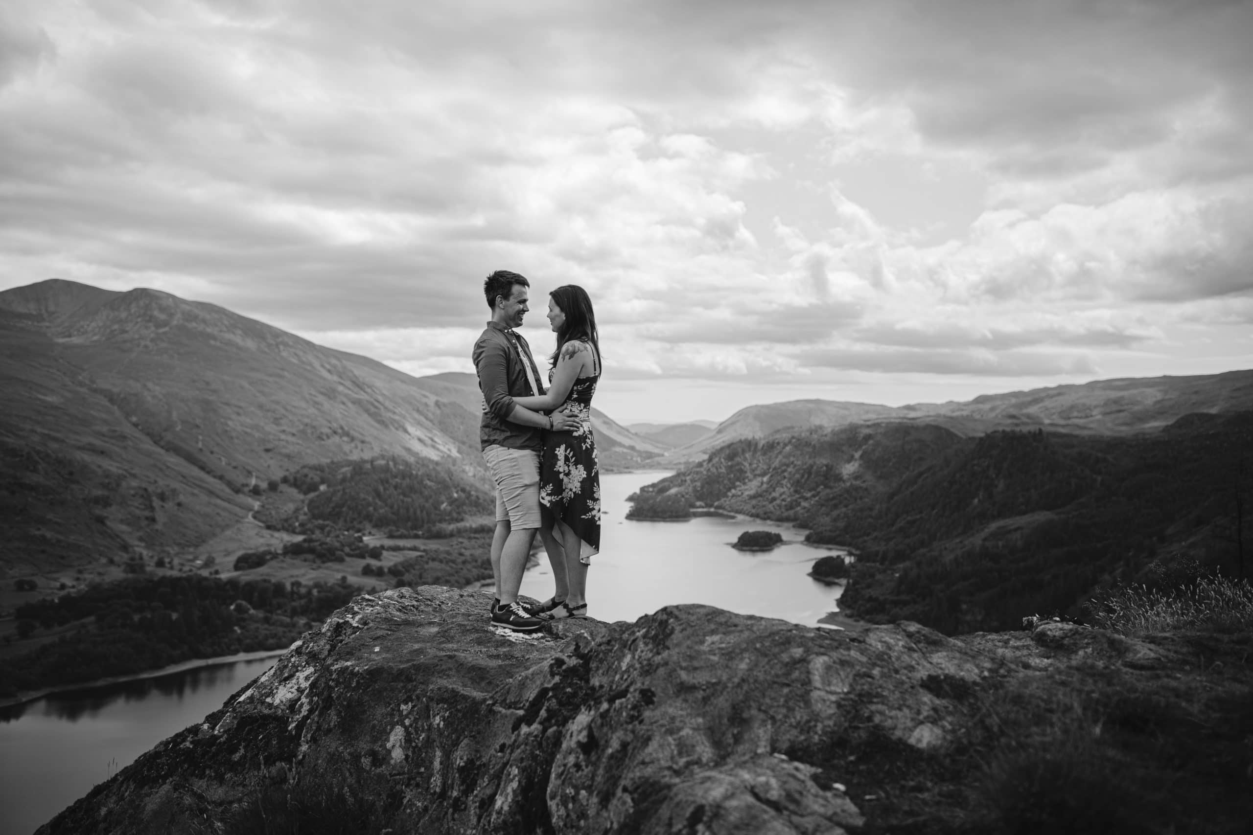 A couple standing on top of a cliff overlooking a lake during their Portrait Session.