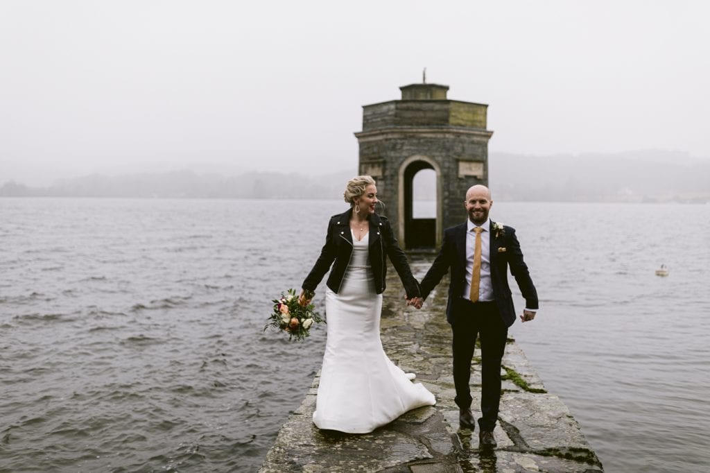 A bride and groom standing on the picturesque Storrs Hall pier near a serene lake.