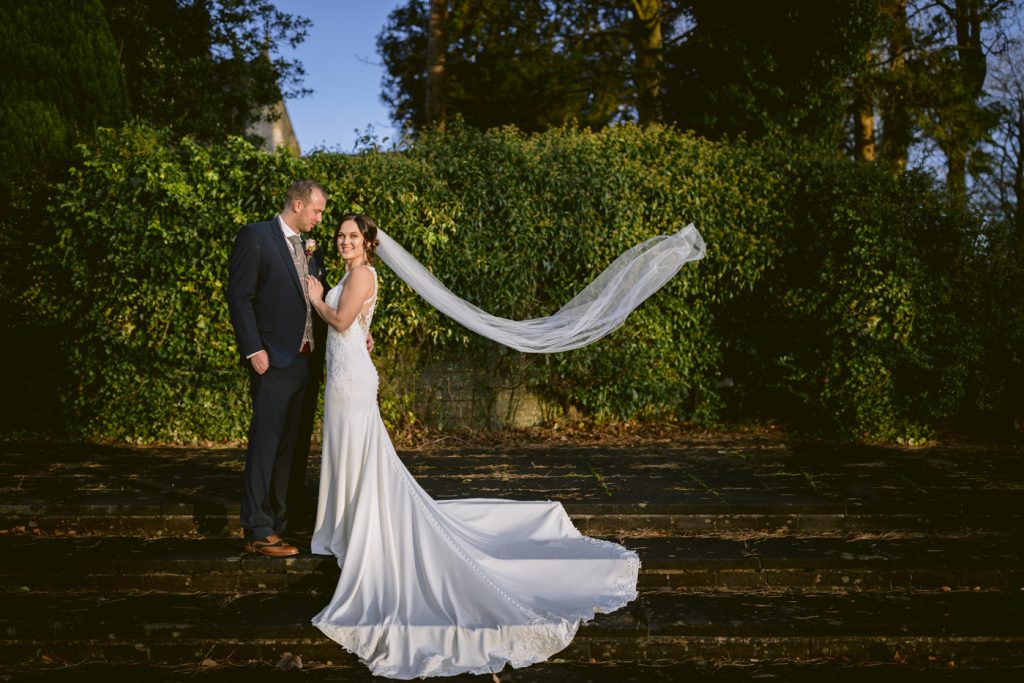 Bride and groom portrait at villa levens kendal on the steps in the weding venue grounds with bride's veil floating