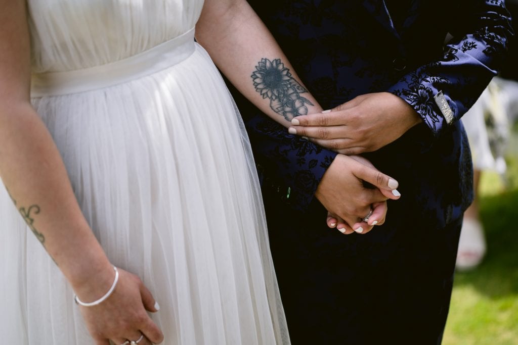 A same-sex couple in the Lake District elopement, holding hands with tattoos on their hands.