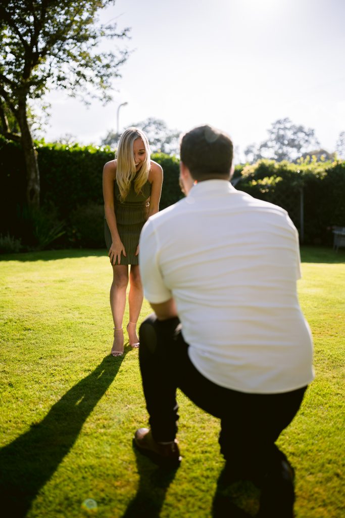 A man kneeling on the grass to propose to a woman.