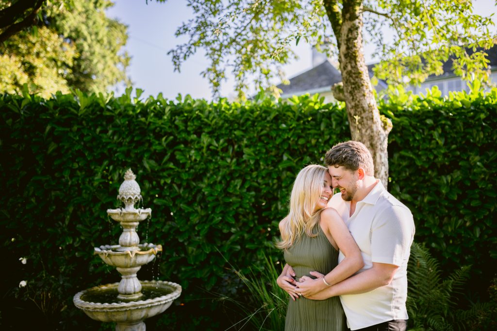 An engaged couple embracing in front of a fountain.