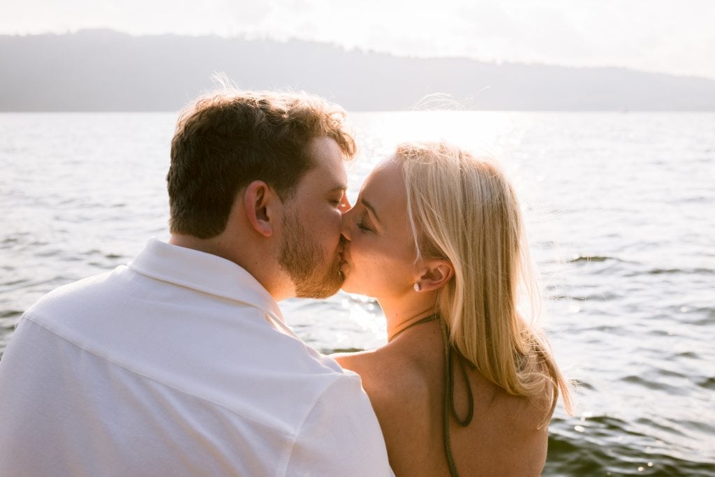 A couple kissing on the shore of a lake.