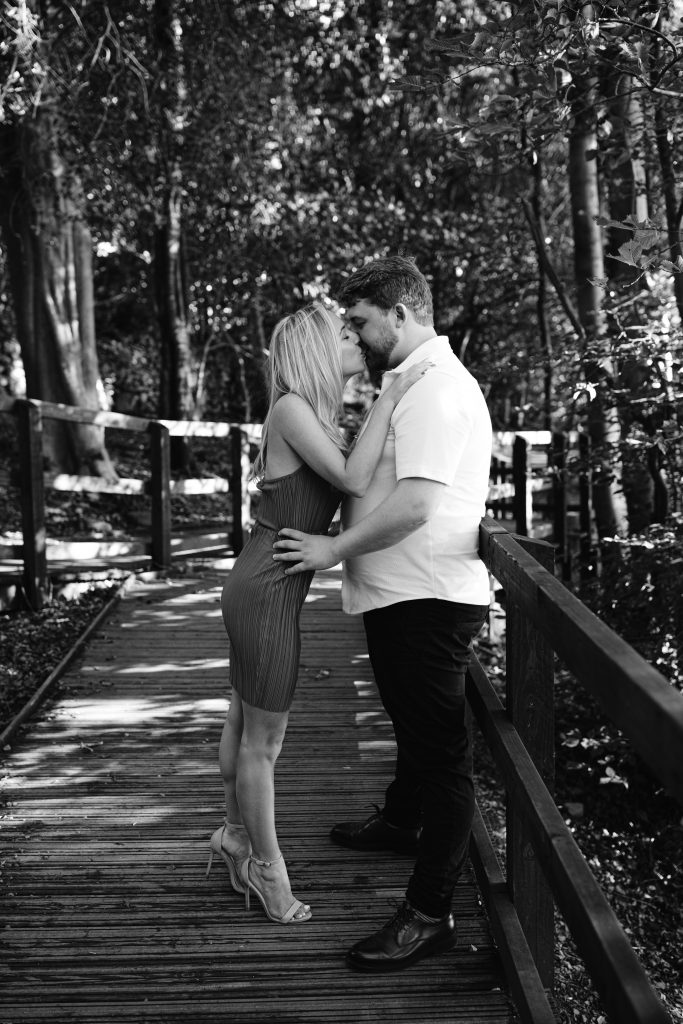 A couple kissing on a wooden bridge in the woods.