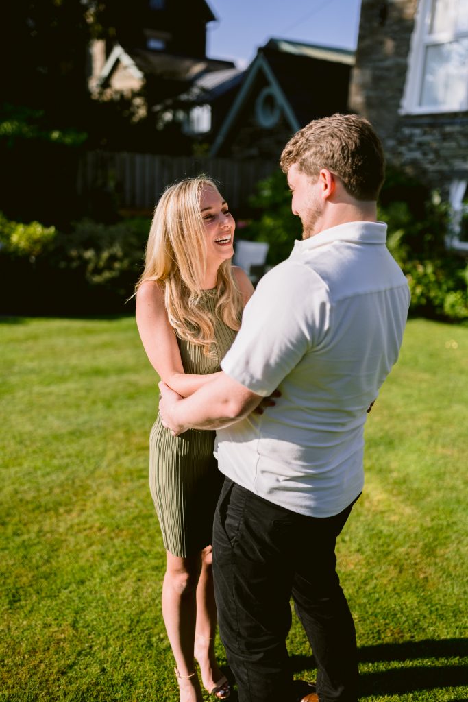 A couple hugging in the grass in front of a house.