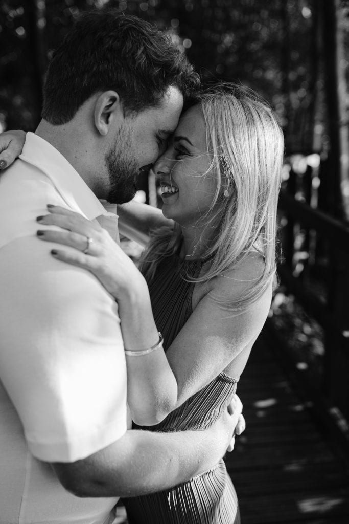 A black and white photo of a couple embracing on a bridge.