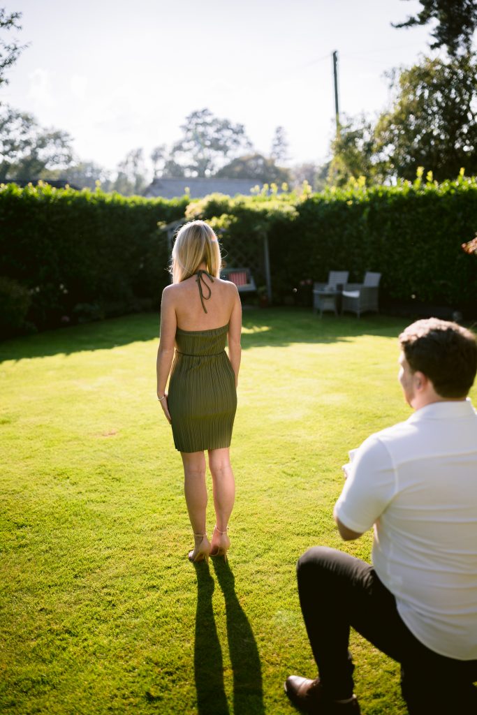 A woman is standing on a lawn with a man standing behind her.