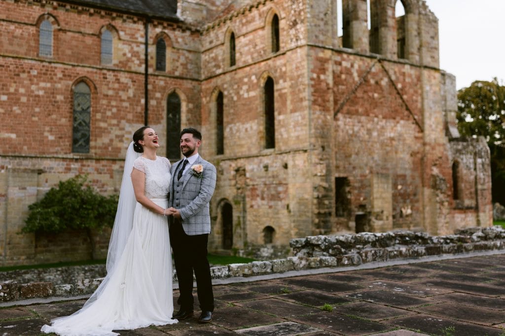 The Wetheral Church Wedding features a beautiful bride and groom, standing regally in front of an old castle as the backdrop.