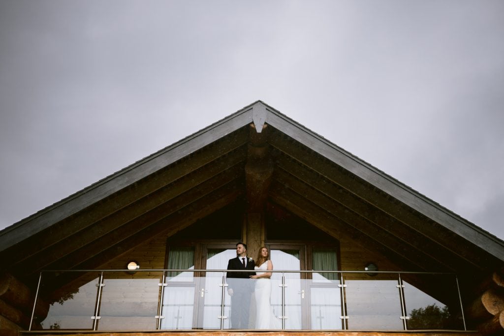 A bride and groom standing on the balcony of a Hidden River Cabins log cabin during their Autumn Elopement.