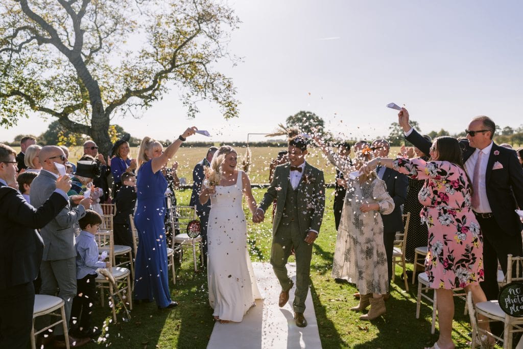 A bride and groom have a joyful outdoor wedding in Yorkshire, walking down the aisle with confetti thrown at them.